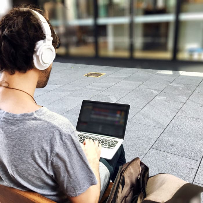 guy sitting on bench wearing headphones and using laptop