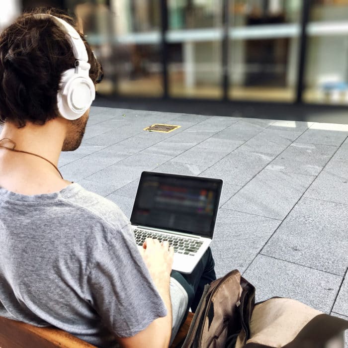 guy sitting on bench wearing headphones and using laptop
